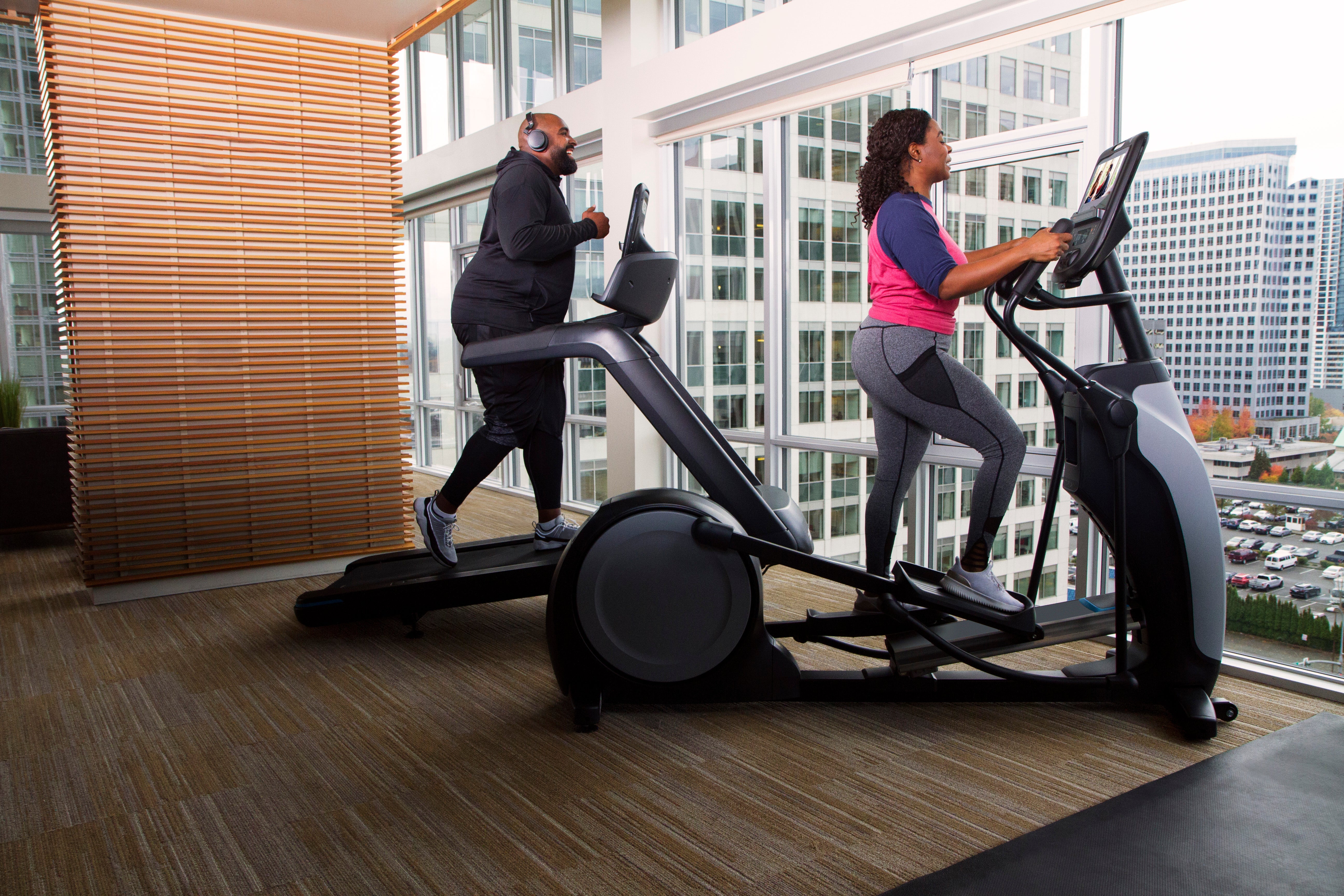 Man exercising on treadmill and woman working out on a Precor elliptical machine in a high-rise apartment building