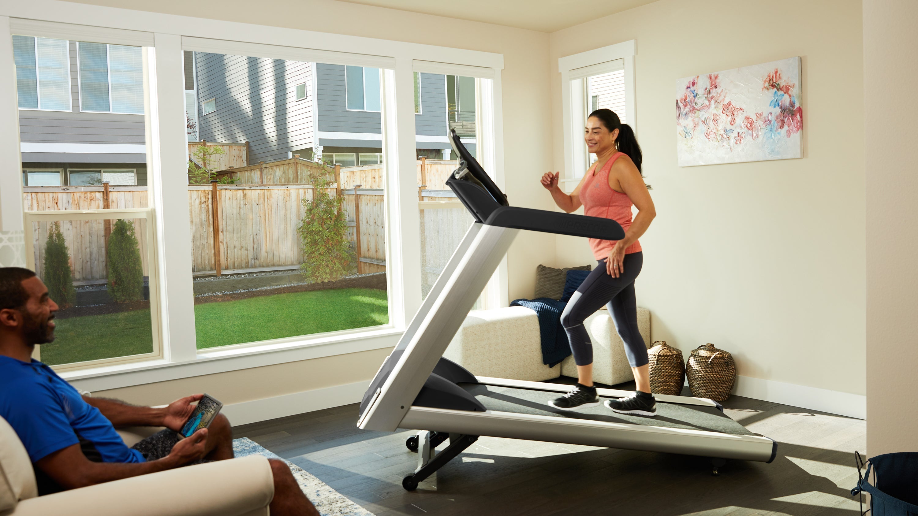 Woman works out on a walking treadmill as a man exercises in the room
