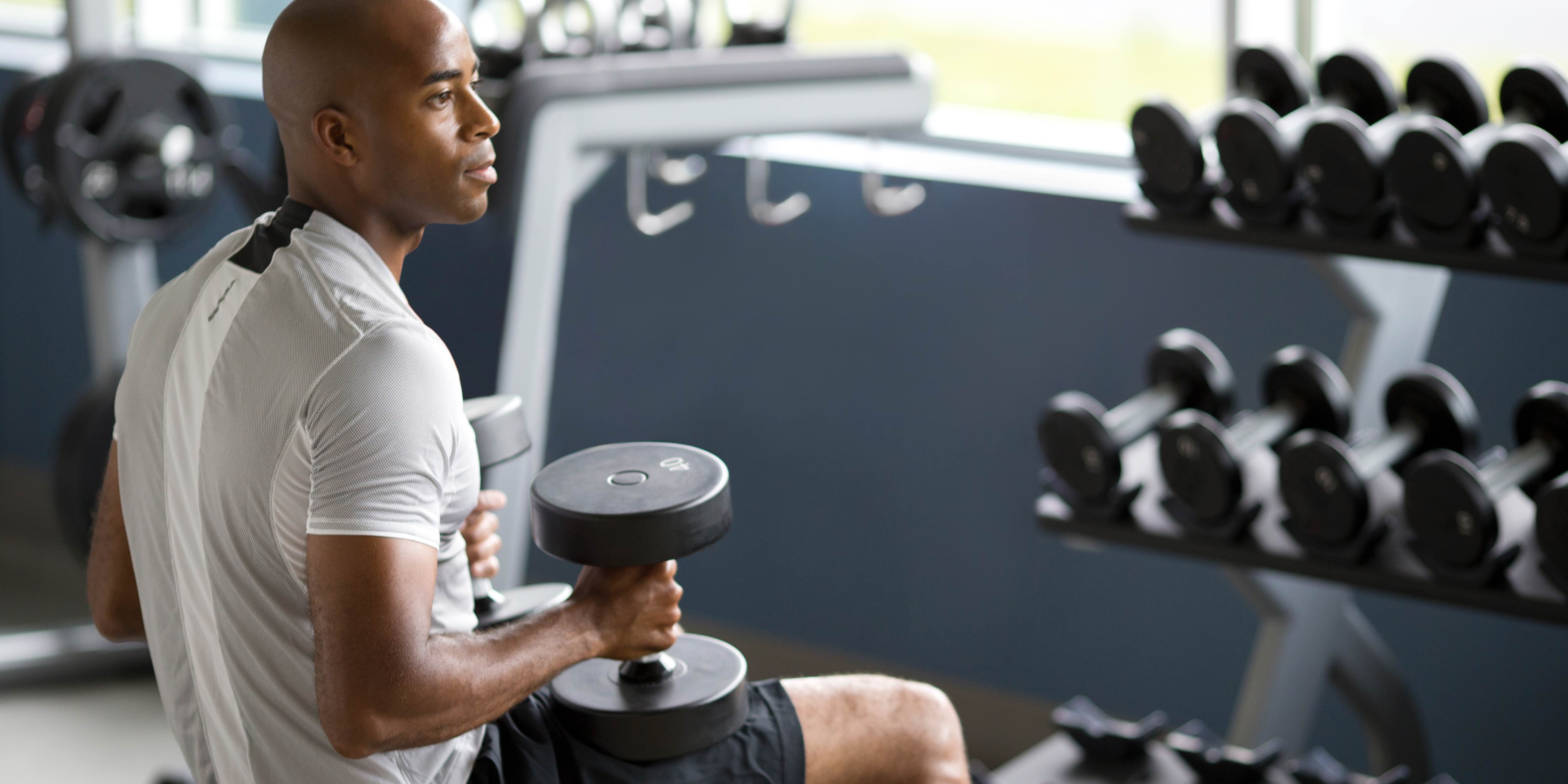 male exerciser strength training with free weights using Precor dumbbell racks