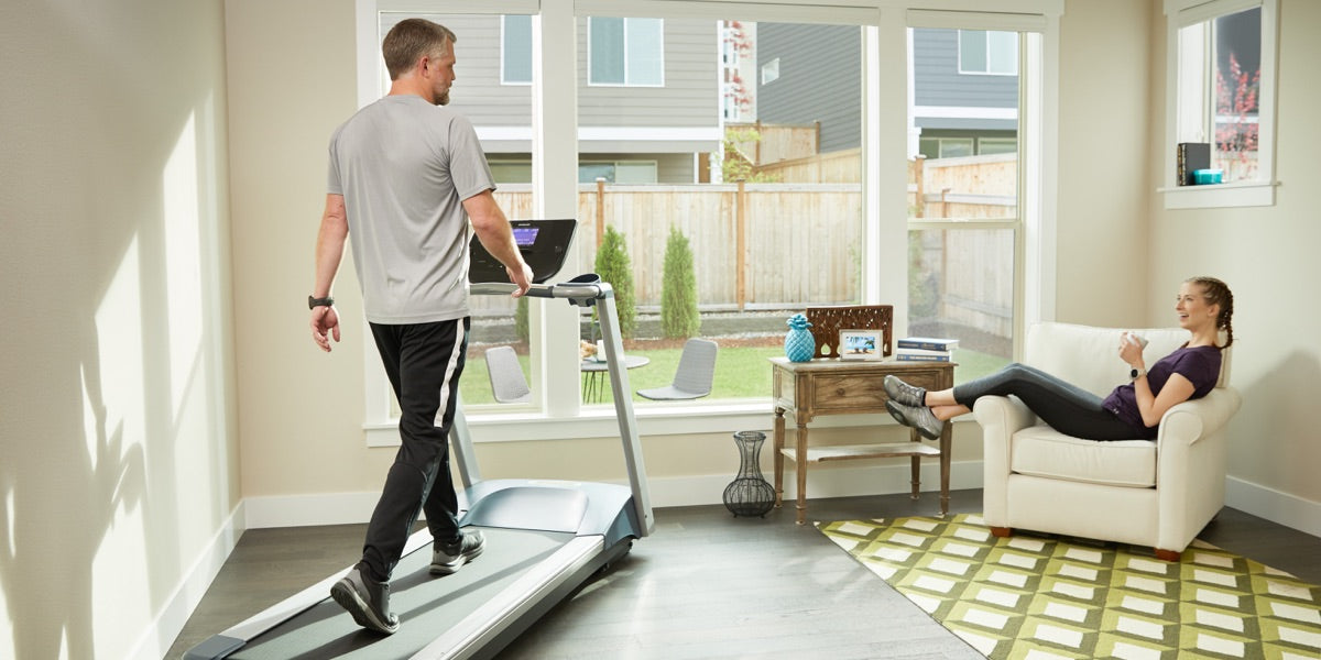 Male walking on his Precor treadmill TRM 211 in his home workout room while a woman hangs out in the chair talking to him
