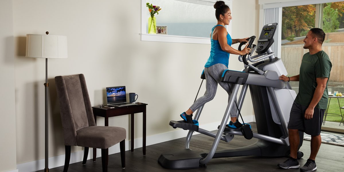 Female working out in her home gym on her Precor AMT 835 Adaptive Motion Trainer, while her husband looks on