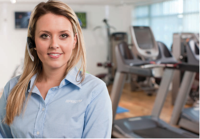 Female Precor customer service representative in front of a row professional gym with Precor TRM 885 treadmills with P80 consoles