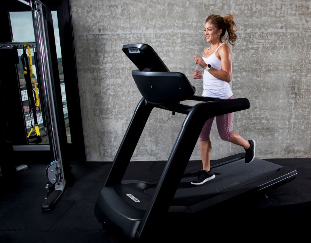 Female running on her Precor TRM 731i interval treadmill in her home gym, that includes a Precor FTS Glide functional strength training system