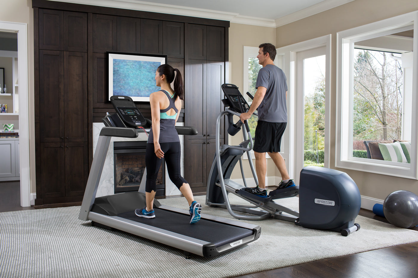 Woman walks on a treadmill, TRM 445, and man is on an elliptical, EFX 447, in their living room