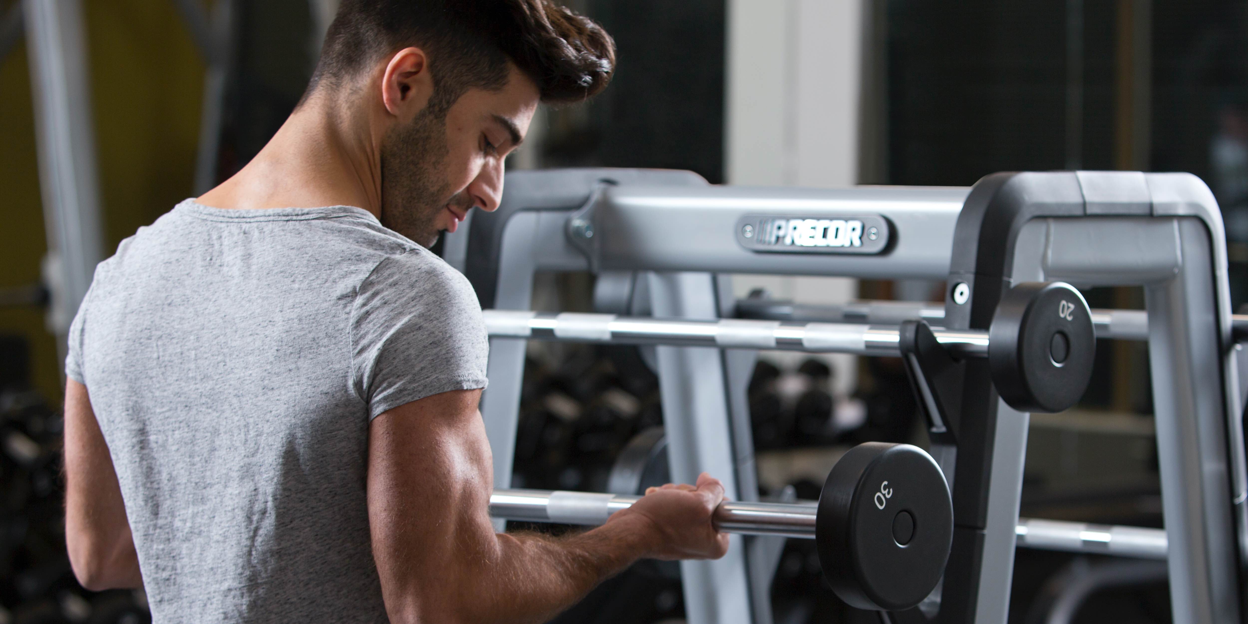 male exerciser strength training with barbell bicep curl using Precor barbell rack